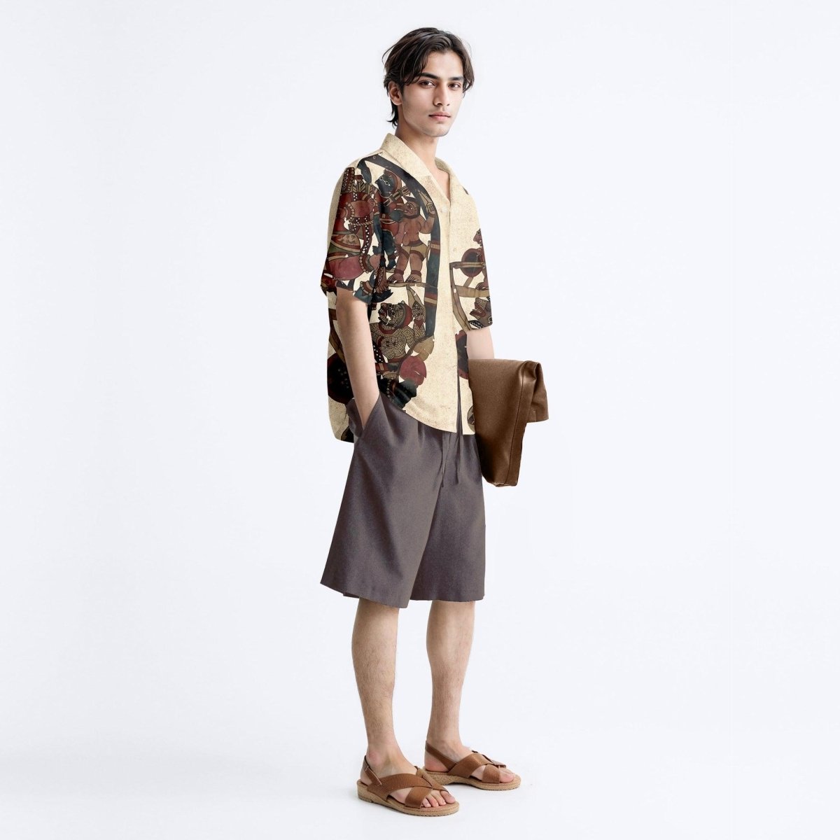 Man wearing the beige Heritage shirt with grey shorts, full length three-quarter view, carrying a jacket